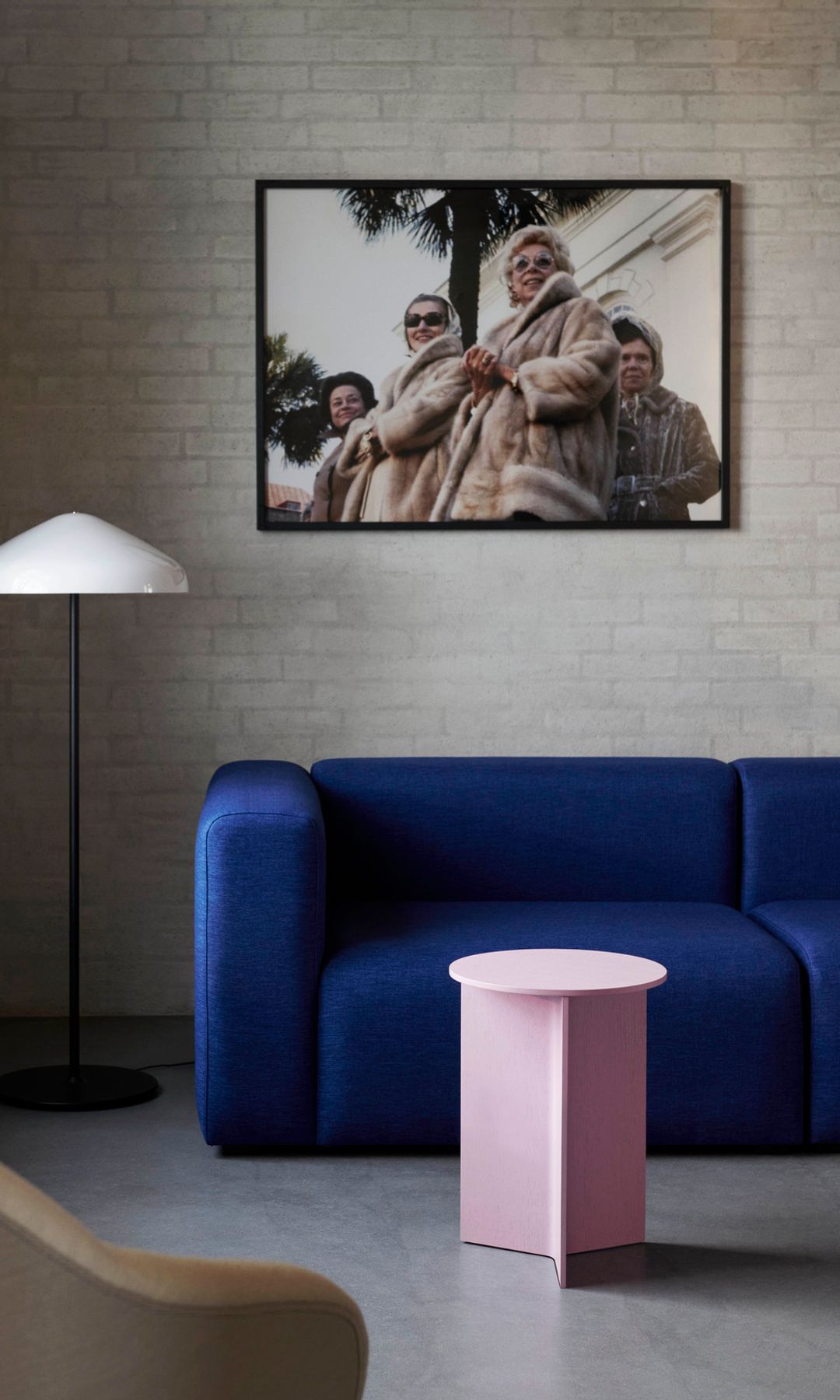 Salón con sofá azul eléctrico, taburete rosa claro, pared de ladrillos, fotografía en la pared del sofá, lámpara de pie 