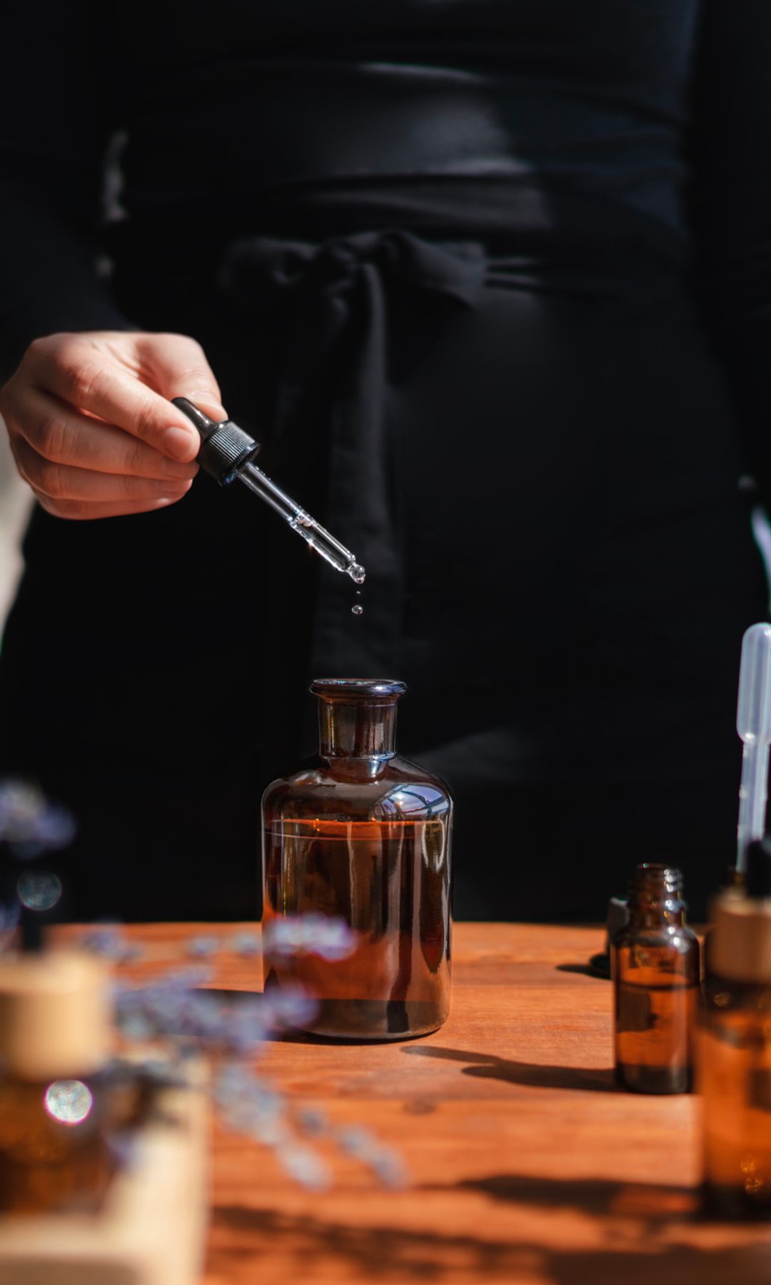 Mujer preparando un líquido aromático para difusor o perfume a partir de aceite esencial de flores.