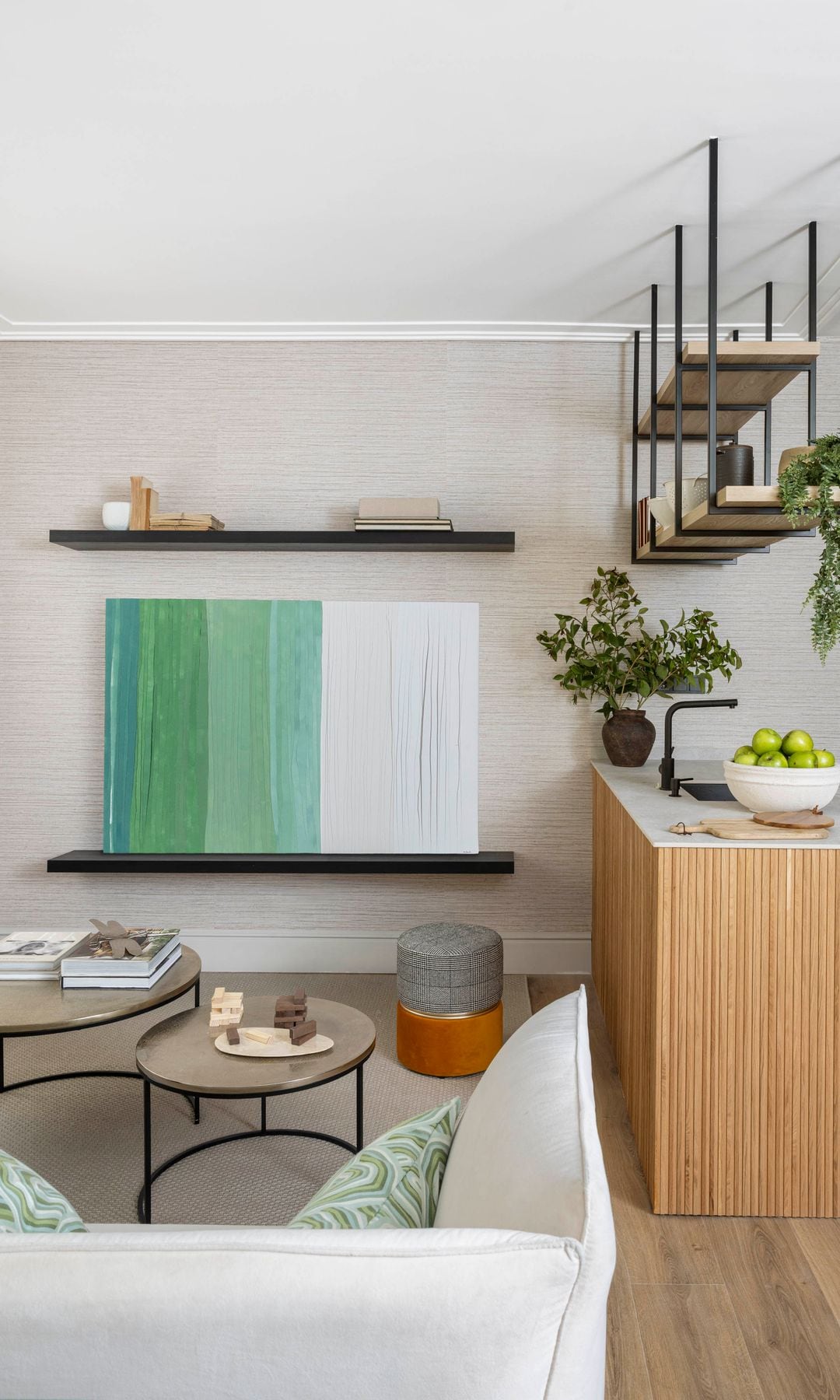 Cocina abierta al salón con isla de madera y encimera blanca, cuadro en la pared, sofá beige, mesas de centro 