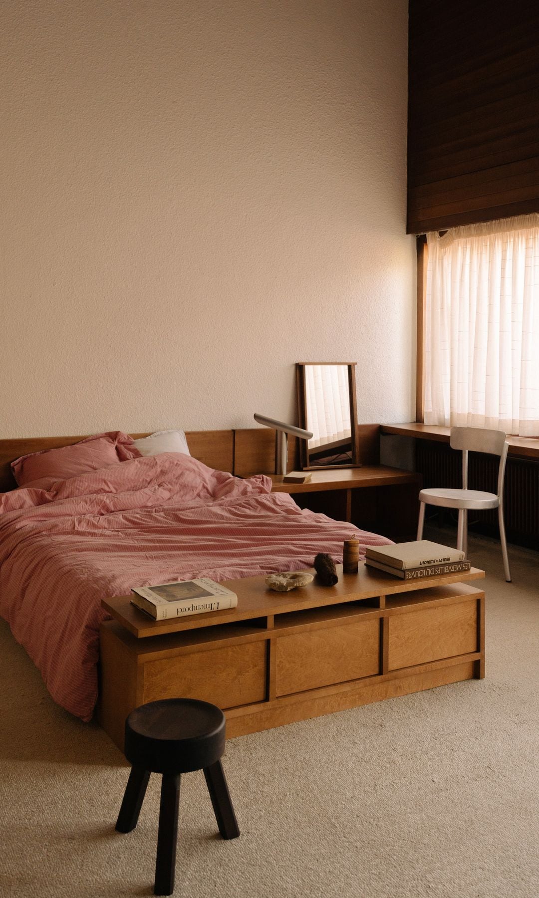 Cama con cabecero de madera, banco de madera a los pies, mesita a modo de tocador, ropa de cama rosa de rayas