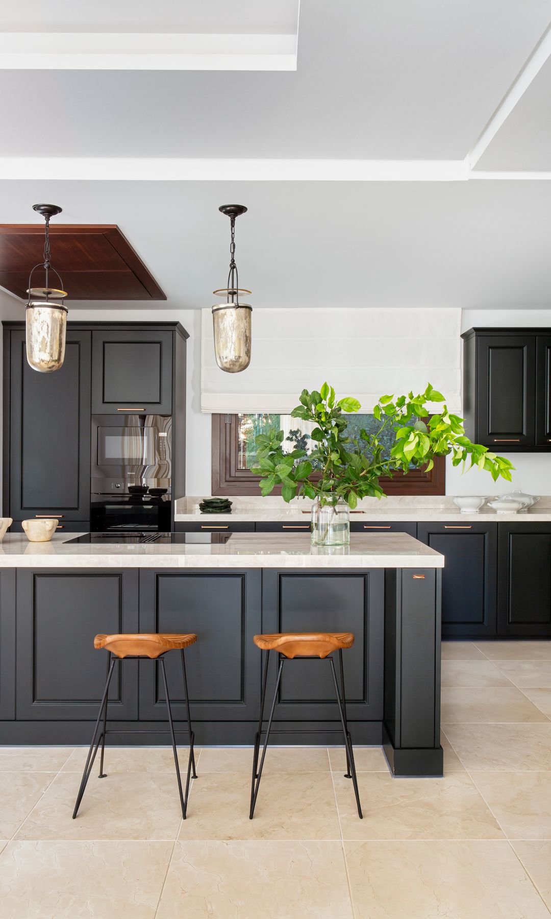 Cocina con isla con muebles negros, encimera blanca, taburetes, lámparas de techo 
