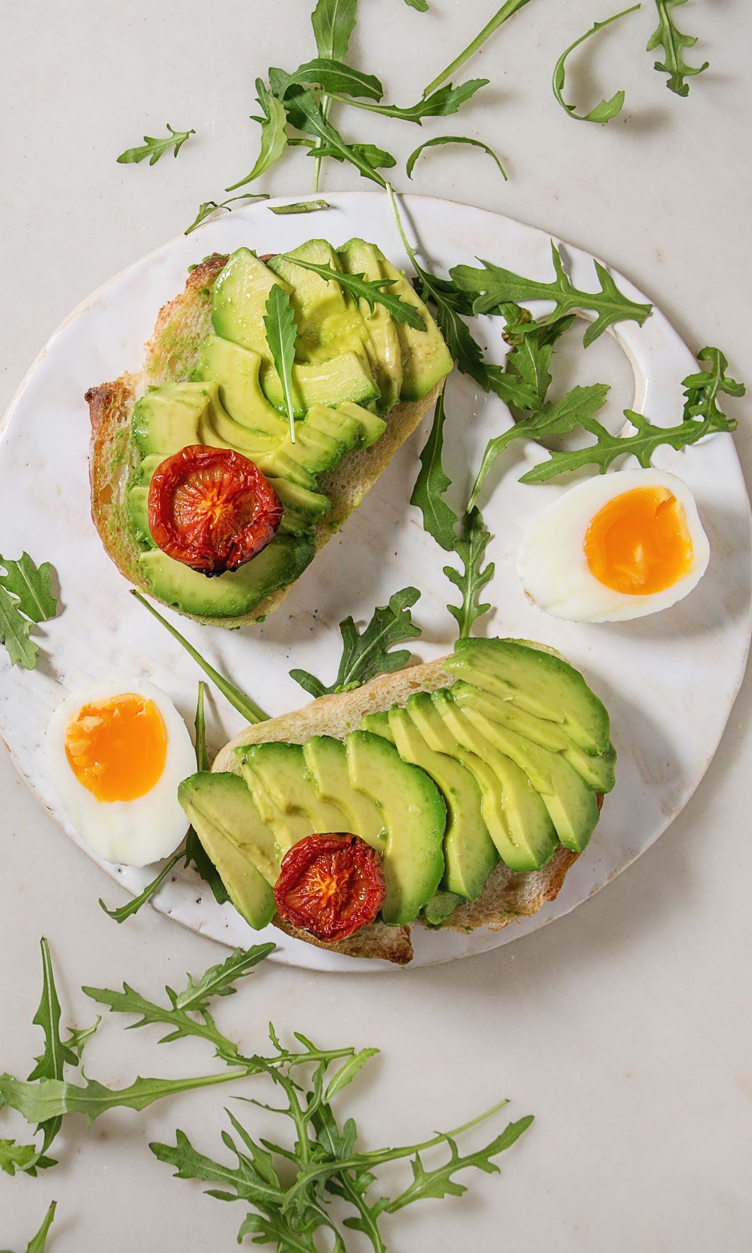 Vegetarian sandwich with sliced avocado. sun dried tomatoes. egg. arugula served on ceramic board over white marble background. Flat lay. space.  (Photo by: Natasha Breen/REDA/Universal Images Group via Getty Images)