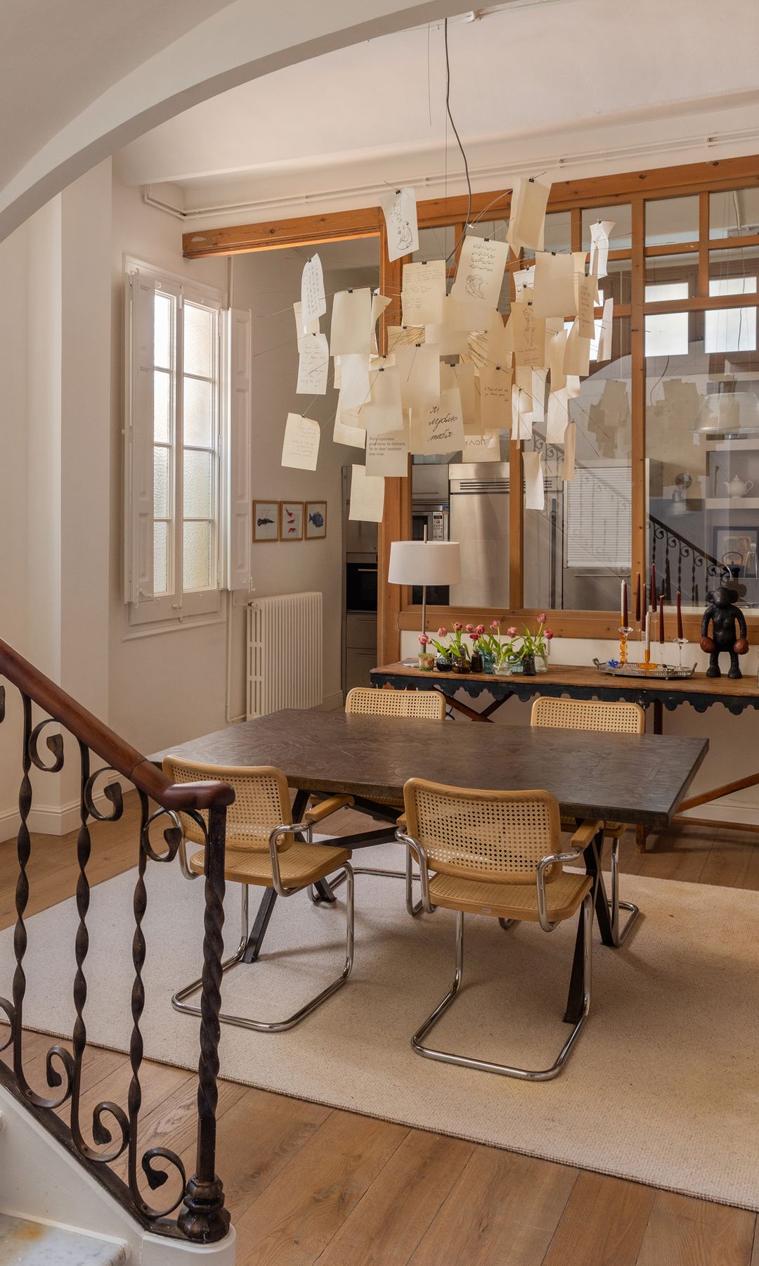 Comedor con alfombra blanca, mesa de madera, sillas Cesca, tabique de cristal con marco de madera, lámpara de techo con mensajes