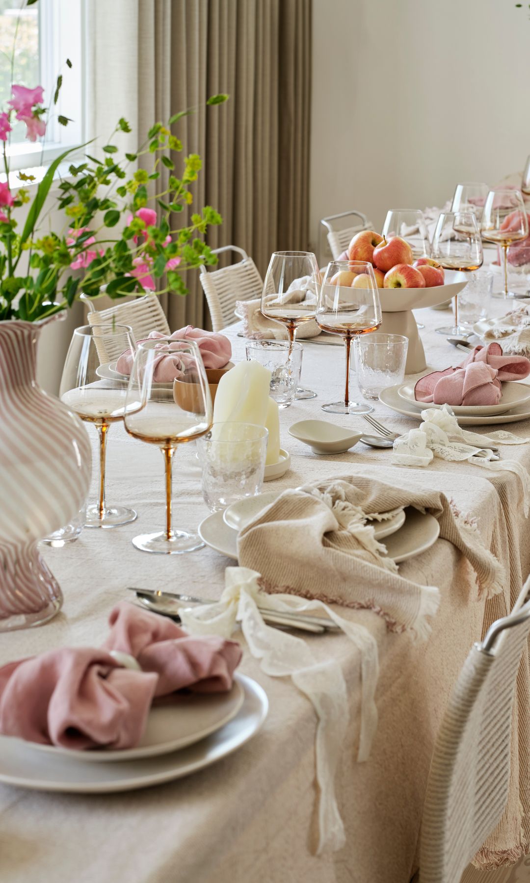 Comedor con mantel de lino beige, copas de vino, vajilla blanca, centros de flores, servilletas de tela  rosa