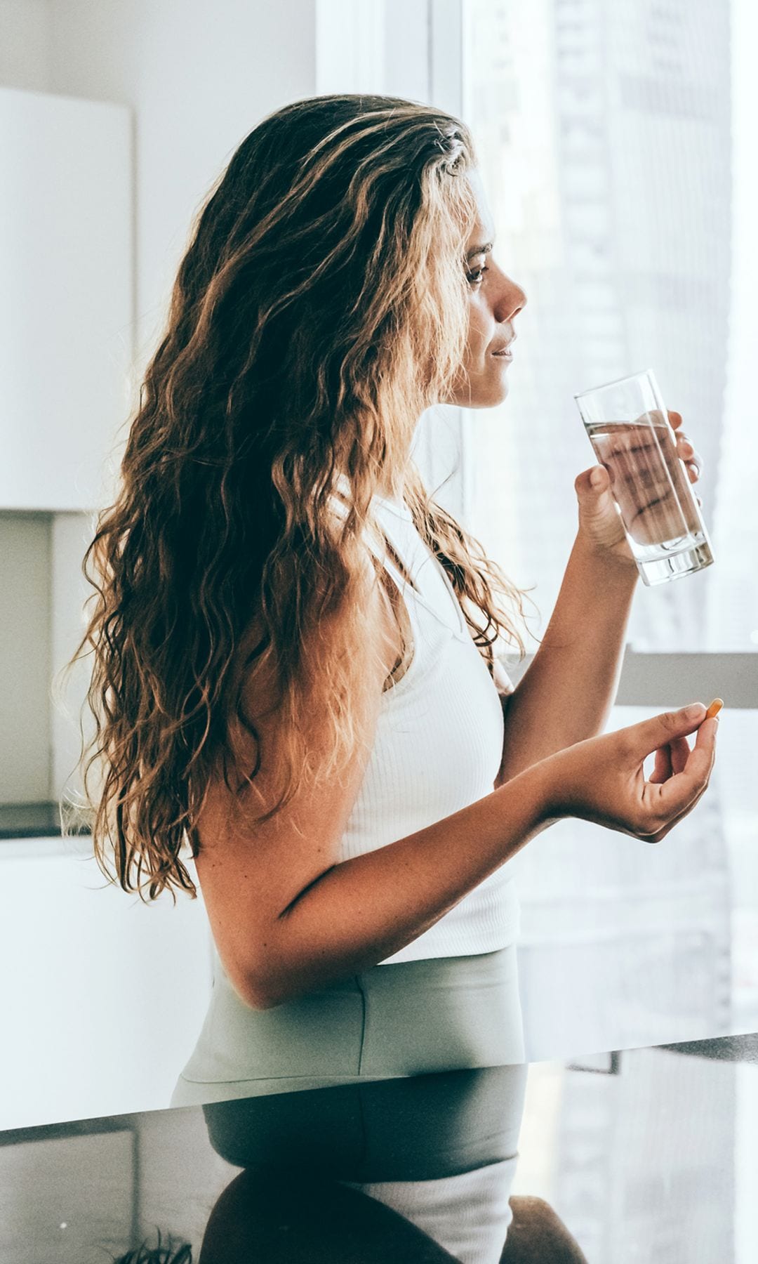 mujer joven tomando suplementos en la cocina