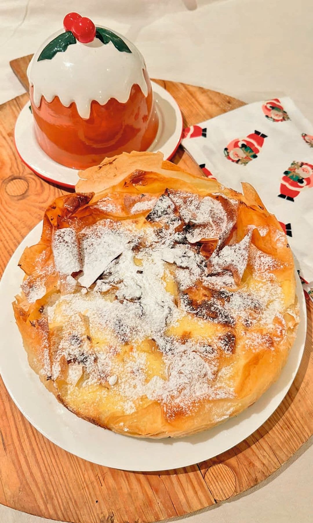 Tarta dorada con azúcar espolvoreada en plato blanco sobre tabla de madera.