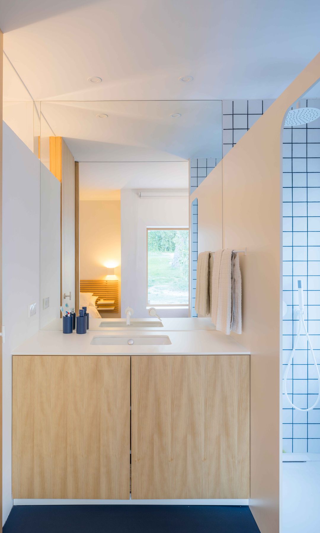 Baño con muebles de madera, espejo, ducha con pared de azulejos blancos con junta negra