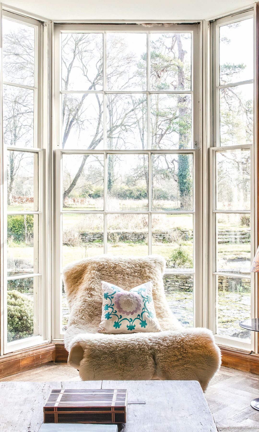 Sala acogedora con ventanas grandes, sillón mullido, y decoración rústica.