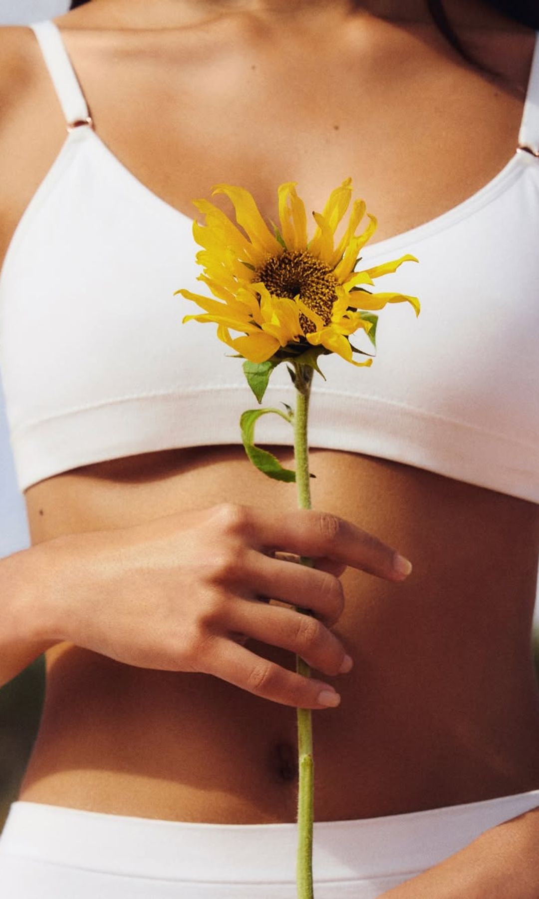 Una mujer con el vientre plano sosteniendo un girasol