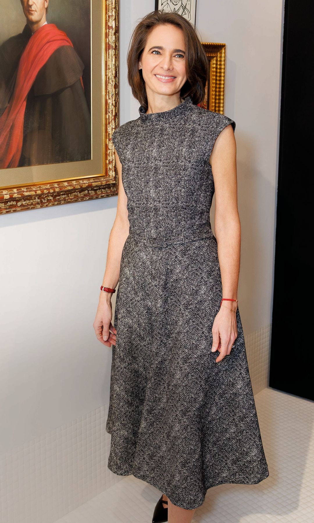 Laurence Debray en vestido gris posando frente a un retrato de Juan Carlos I.