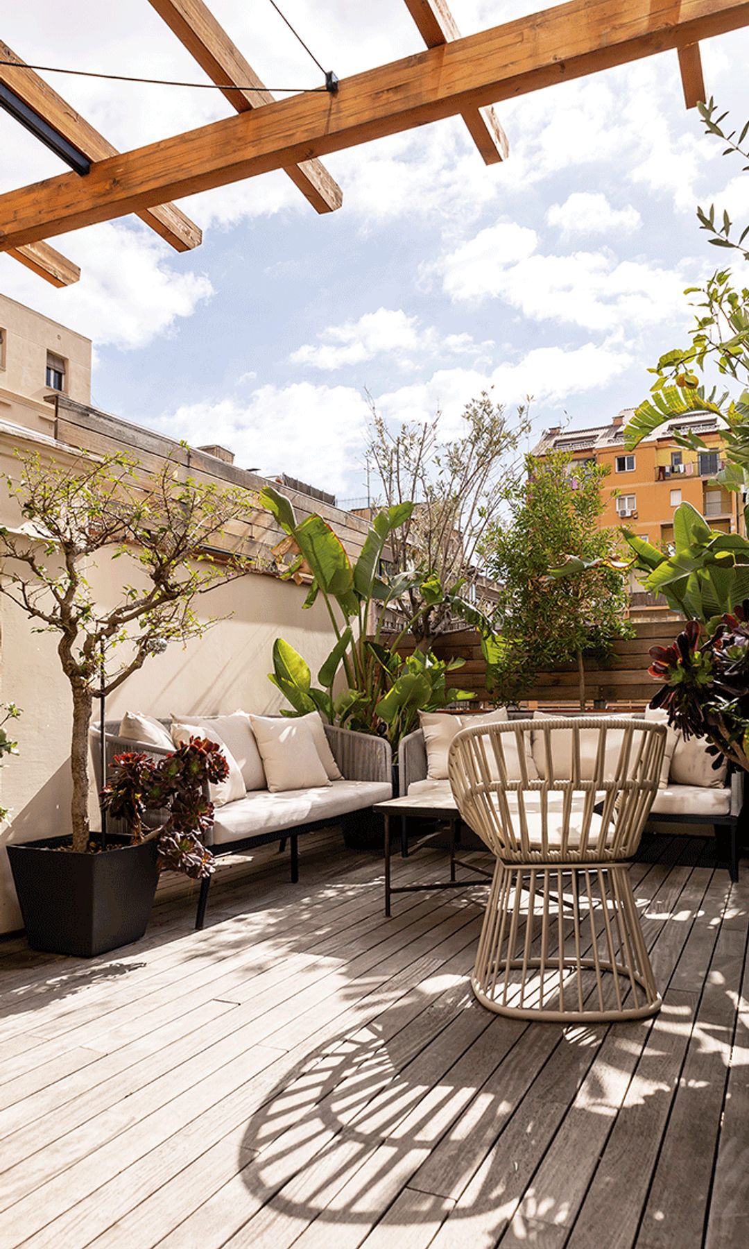 Terraza con suelo de madera, sofás, pérgola de madera, plantas en maceta