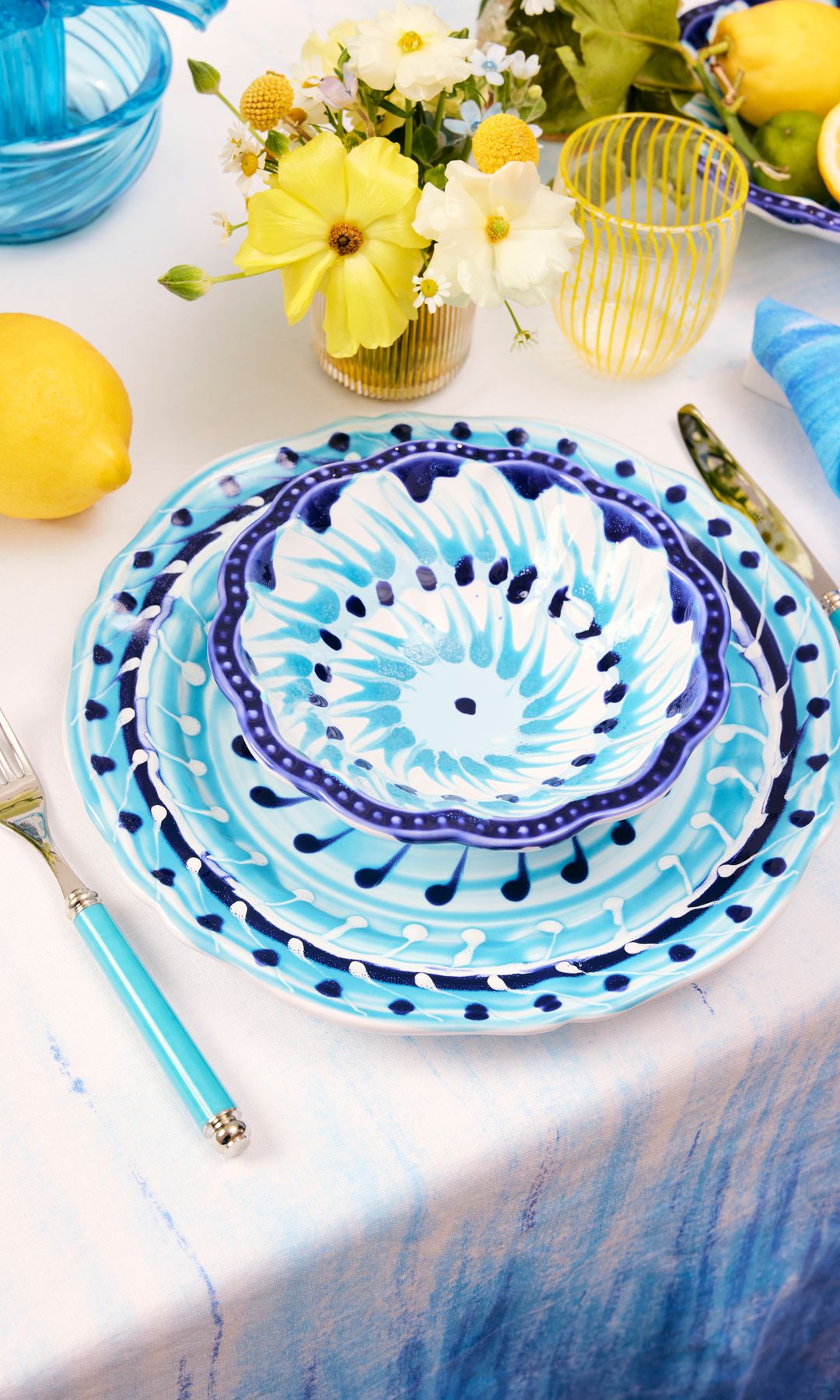 mesa de verano con vajilla de flores azules, cubiertos azules, limones, centro de flores amarillas, vasos amarillos