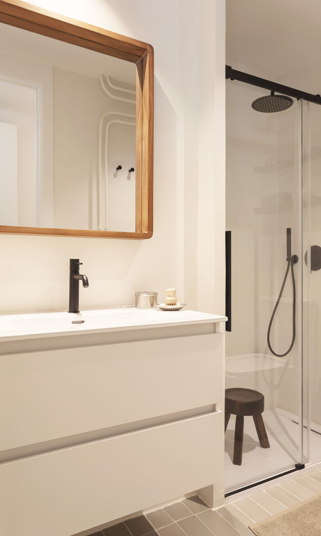 Baño con ducha con plato a ras de suelo, mampara con perfil negro, mueble de lavabo blanco, espejo con el marco de madera