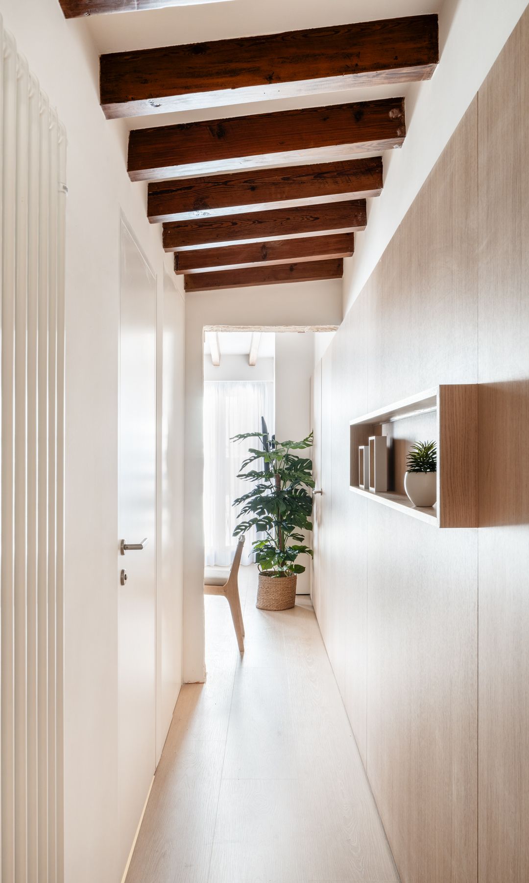 Pasillo distribuidor con pared de madera, estante de madera con plantas y adornos, suelo de madera