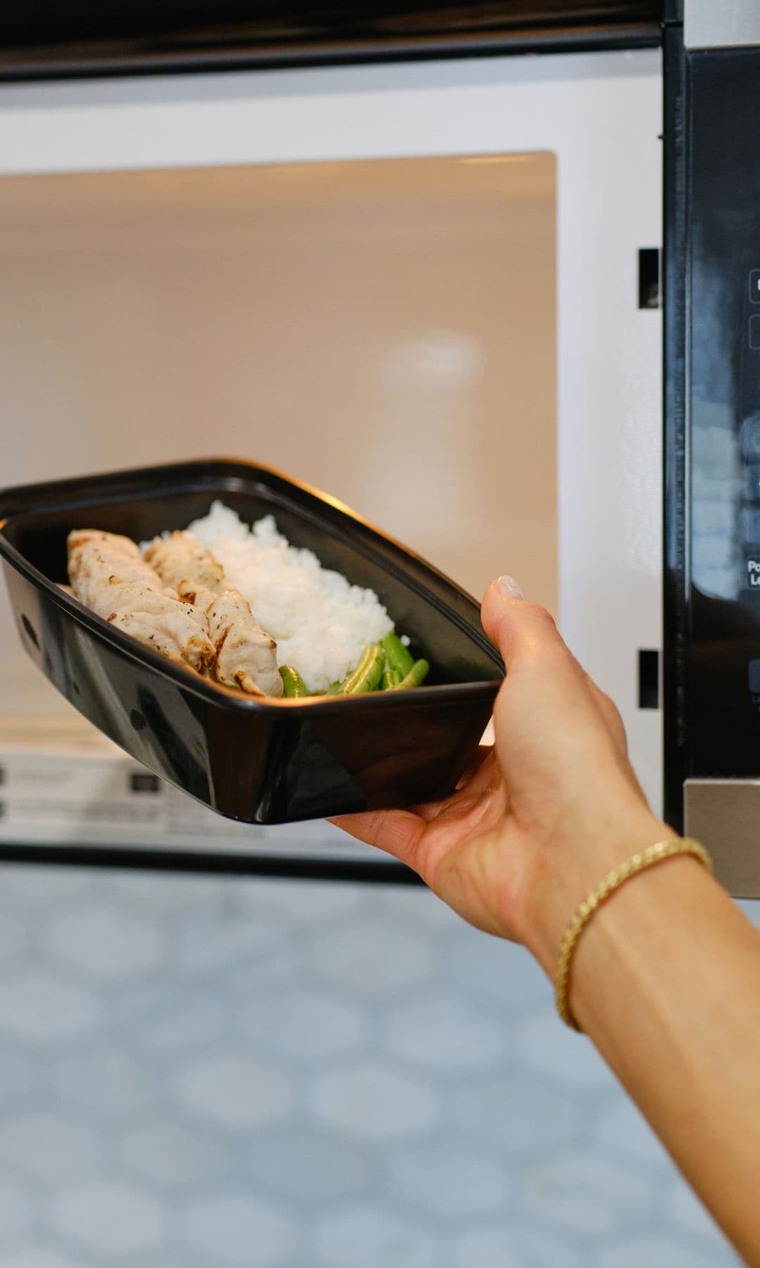 Una mujer metiendo un táper en el microondas