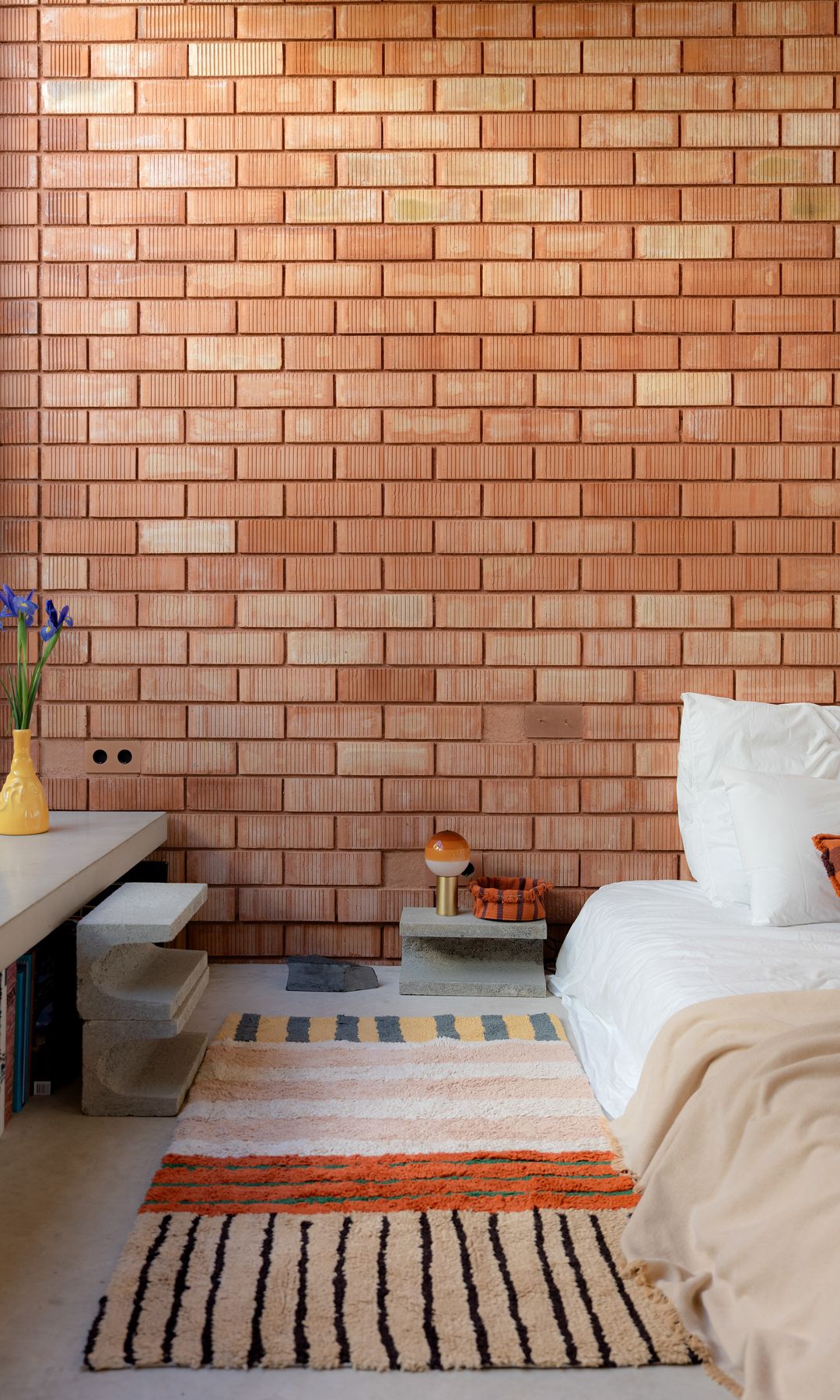 Dormitorio con pared de ladrillo, mueble bajo la ventana, alfombra de lana