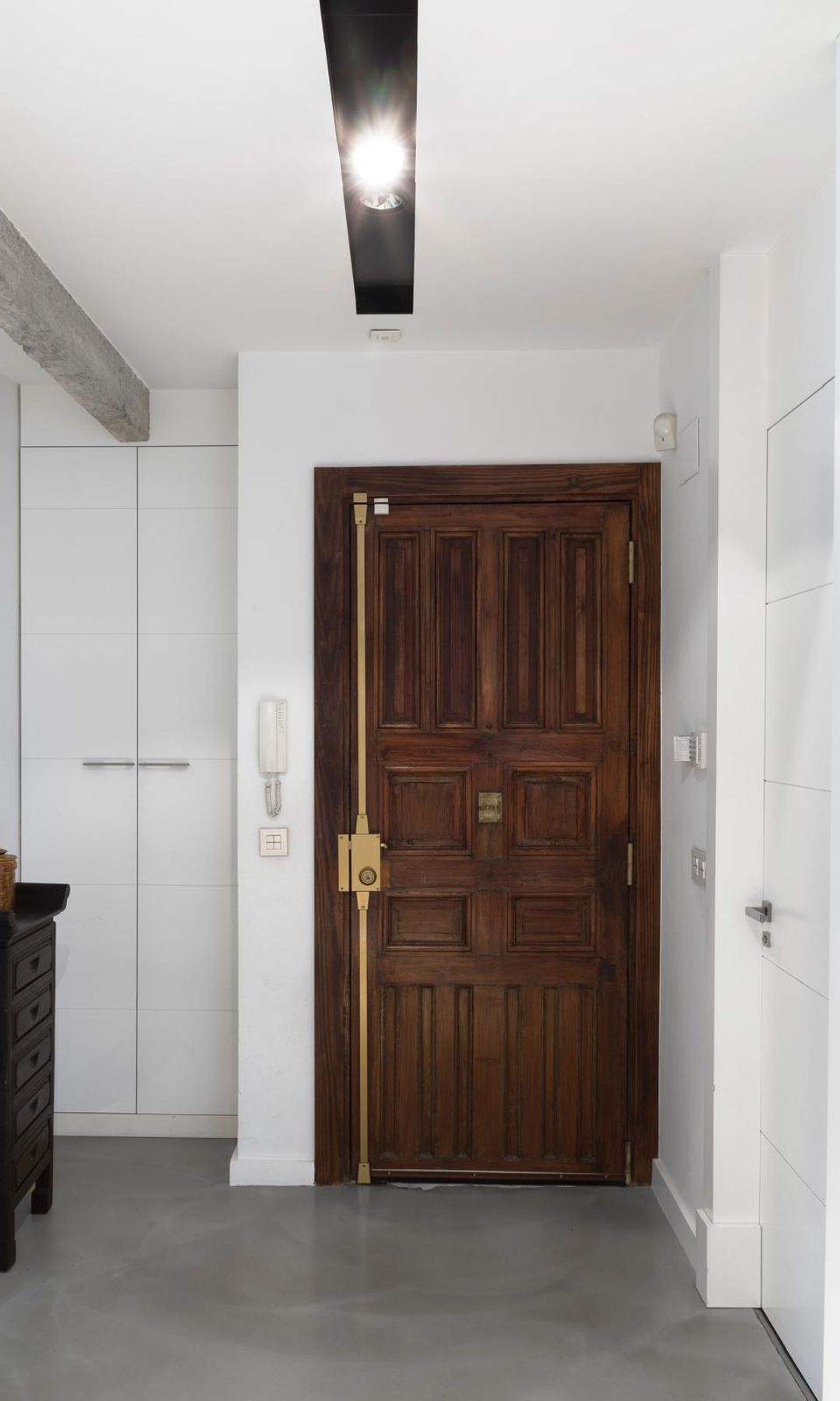 Entrada casa con puerta de madera de seguridad, pasillo con puertas blancas, consola negra