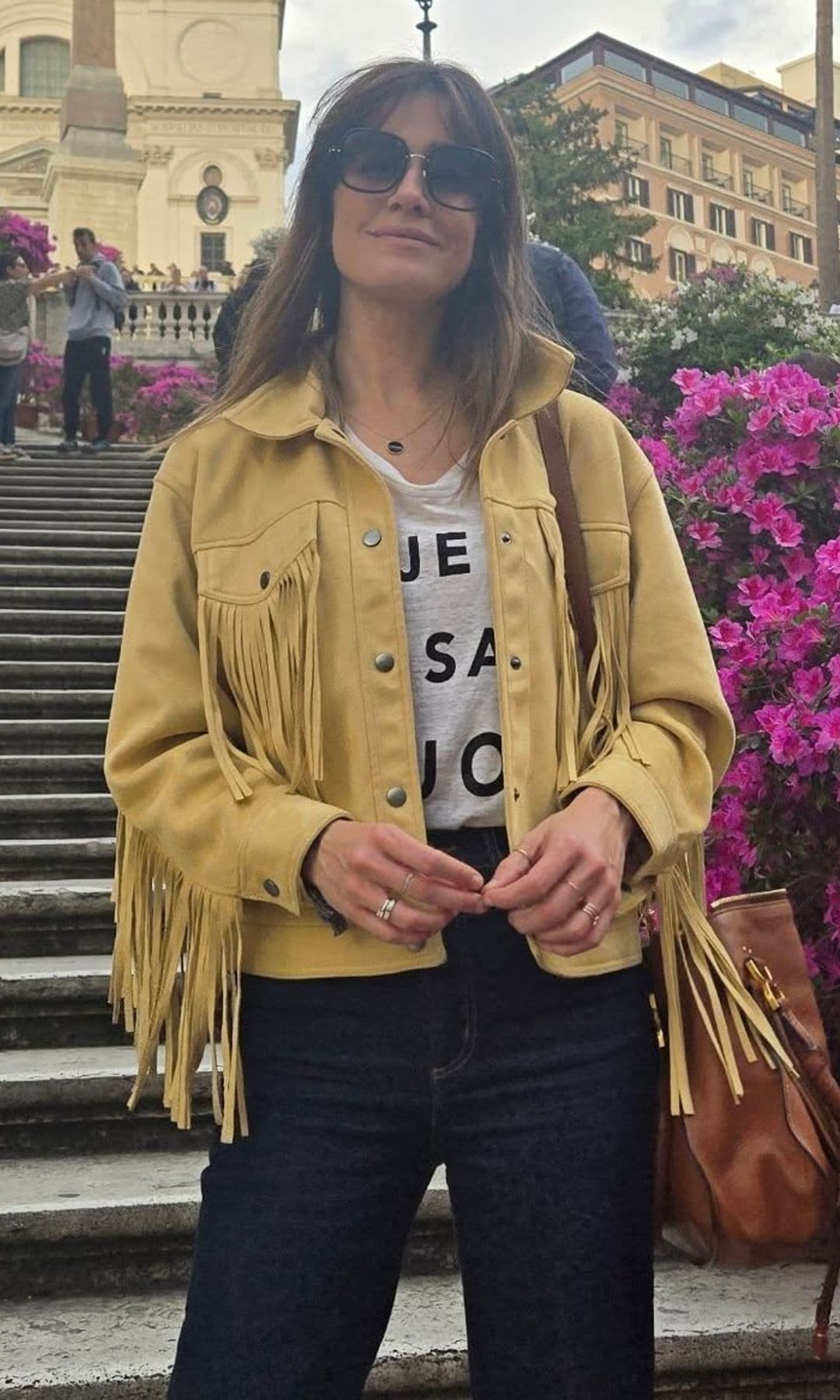 Isabel Jiménez con pantalones negros, camiseta con mensaje, cazadora amarilla y gafas de sol 'oversized'