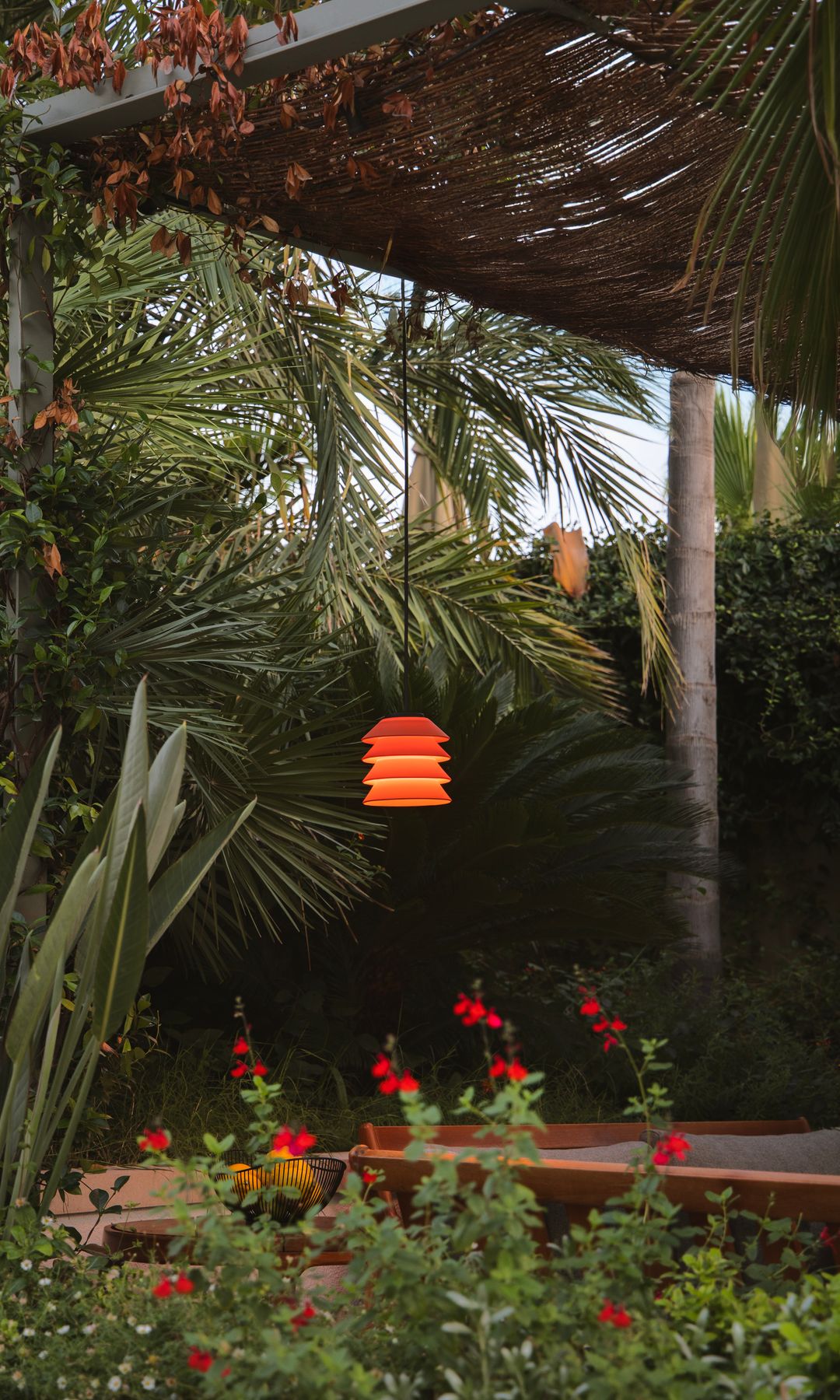 Jardín tropical con palmeras, arbustos con flores rojas, lámparas encendidas