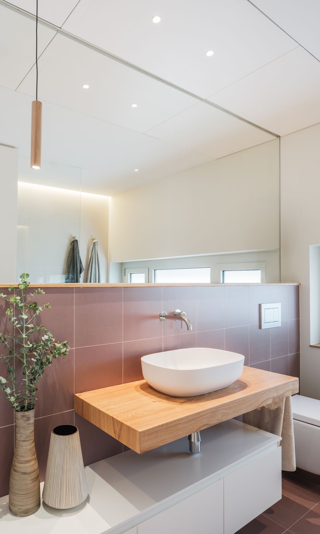 Baño con azulejos en suelo y pared, espejo XL sobre la zona del lavabo, mueble blanco y lavabo sobre encimera
