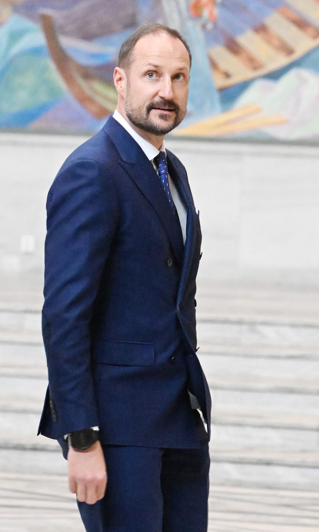 Plano medio de Haakon de Noruega con traje azul marino atendiendo una visita