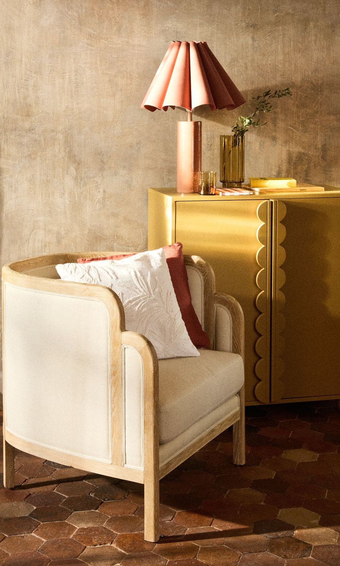 Butaca blanca y mueble bajo amarillo con puertas, suelo de barro, lámpara de sobremesa con pantalla en ondas, cojines, suelo de barro