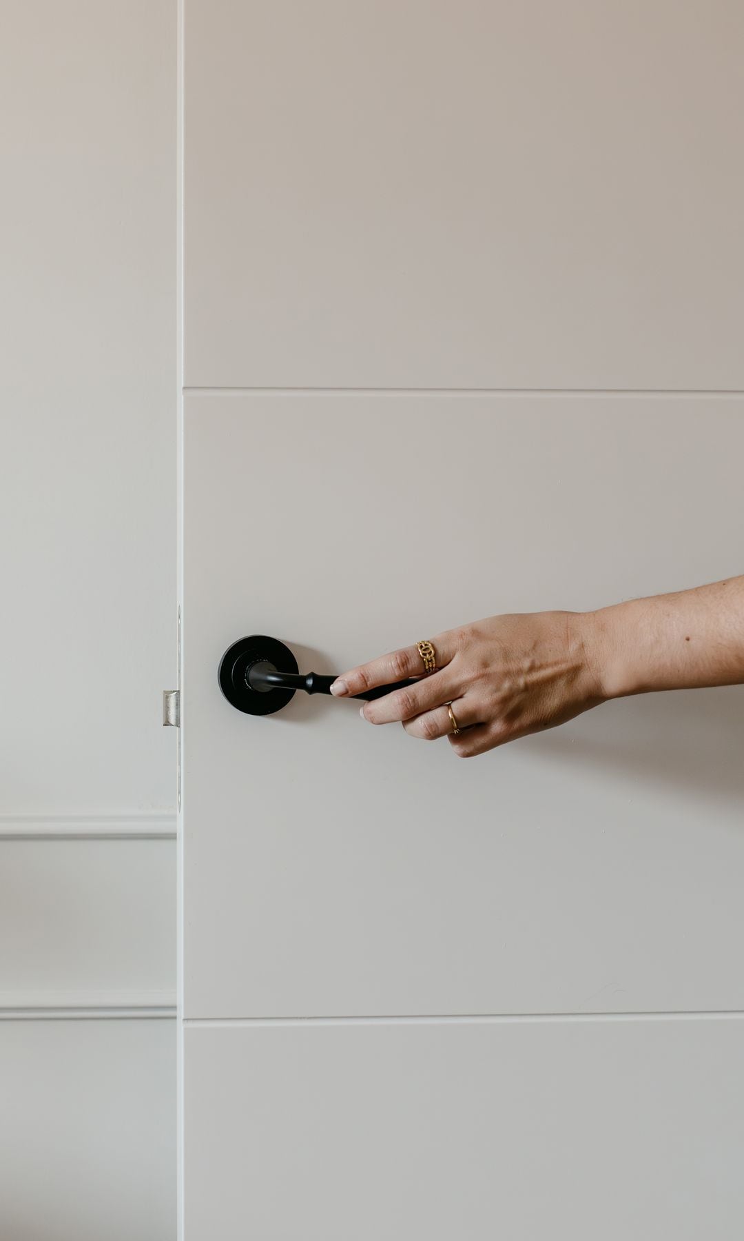 Mano abriendo puerta blanca con manilla negra 