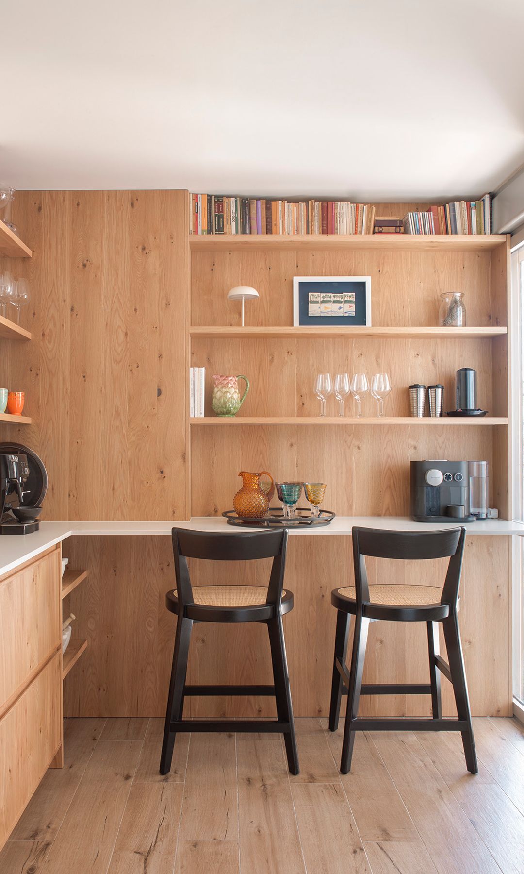 Cocina de madera con barra de desayunos con baldas de madera, taburetes altos negros, cafetera y tazas