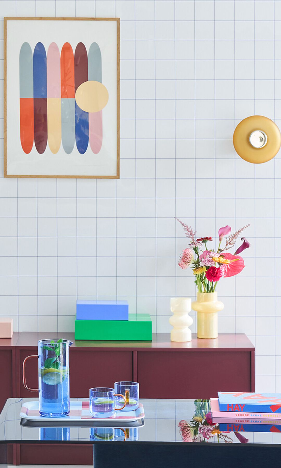 Comedor con pared de azulejos, aparador burdeos, cuadros de colores, jarra con vasos azules 
