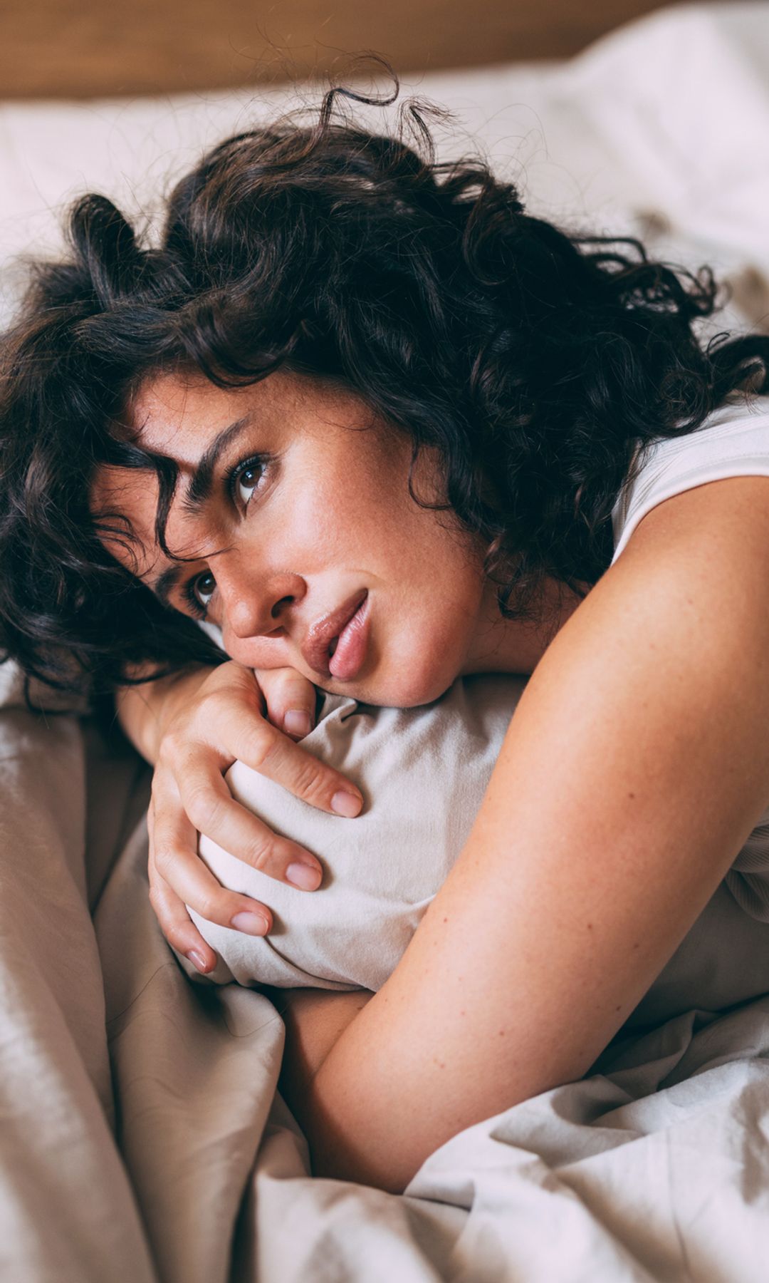 Mujer con el cabello negro y rizado tumbada en la cama con cara pensativa