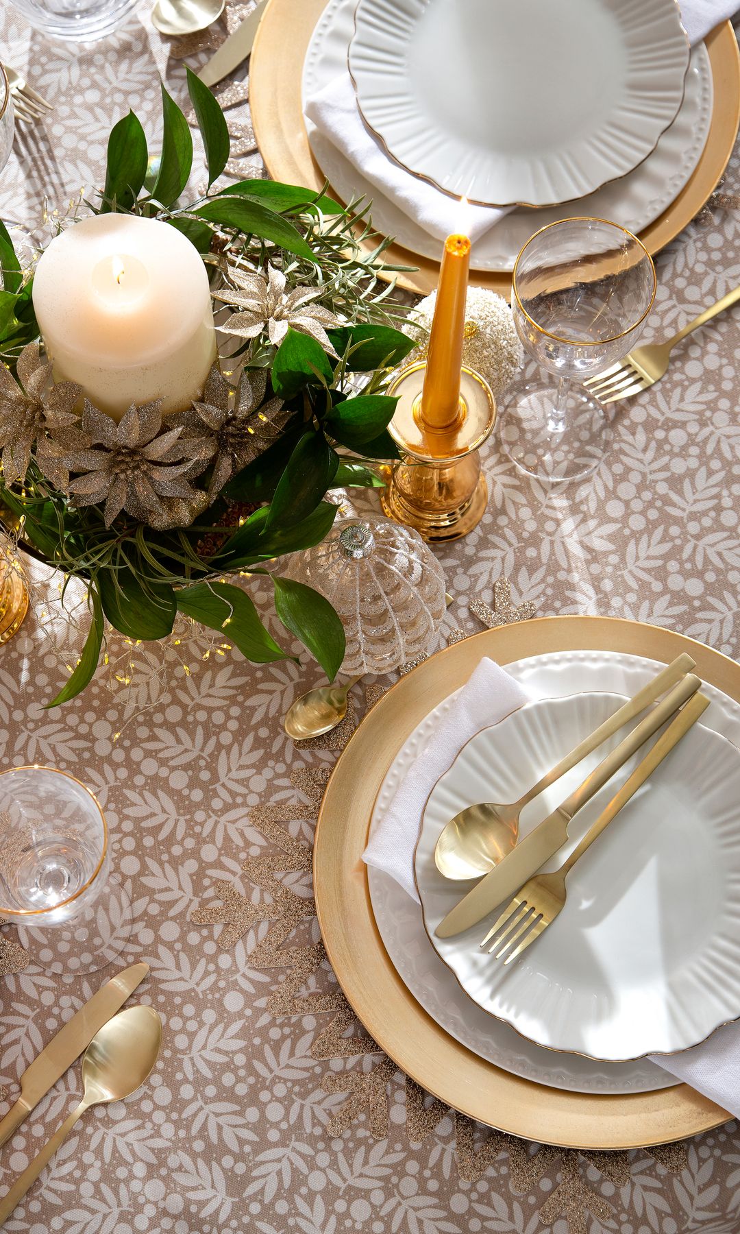 Mesa de Navidad con mantel beige, bajoplatos dorados, cubiertos dorados, candelabros dorados, vajilla blanca con el filo dorado 