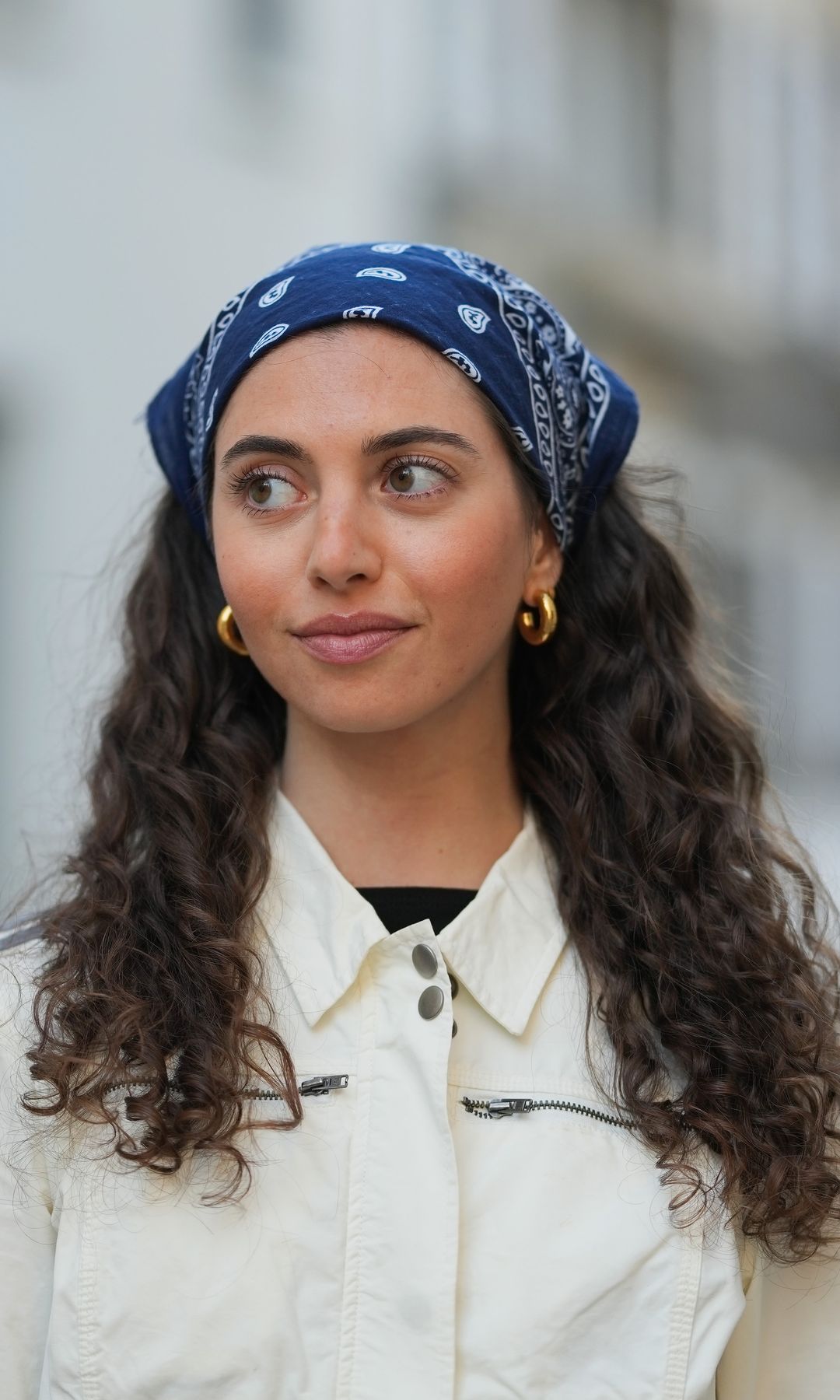 PARIS, FRANCE - APRIL 14: Amanda Derhy wears a blue scarf bandanna over the head with printed patterns, earrings, a white Adidas jacket with stripes on the sleeves, during a street style fashion photo session, on April 14, 2026 in Paris, France
