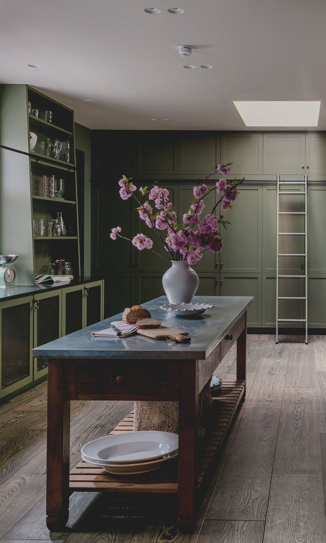 Cocina con muebles verdes y mesa de trabajo con el sobre de mármol, cajones y barra inferior, suelo de madera, escalera 