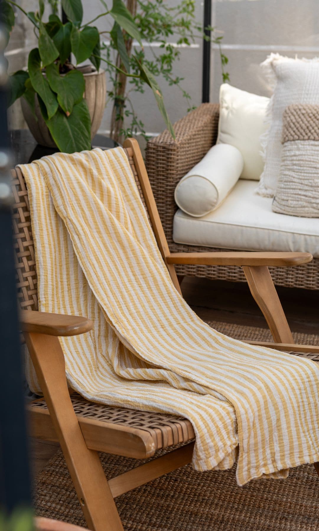 Terraza con silla de fibras vegetales y madera, toalla de rayas amarillas y blancas, sofá con asientos blancos