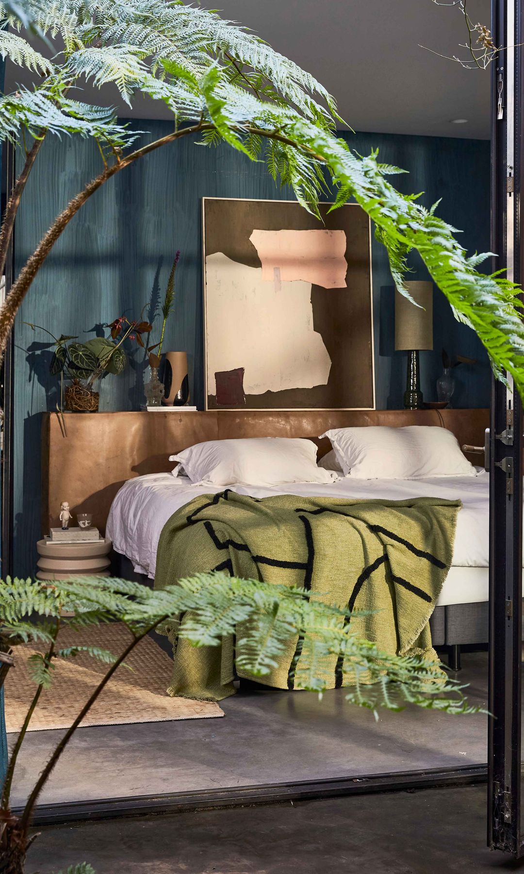 Dormitorio con salida al jardín, manta verde, plantas, cuadro en el cabecero, cabecero de madera, alfombra