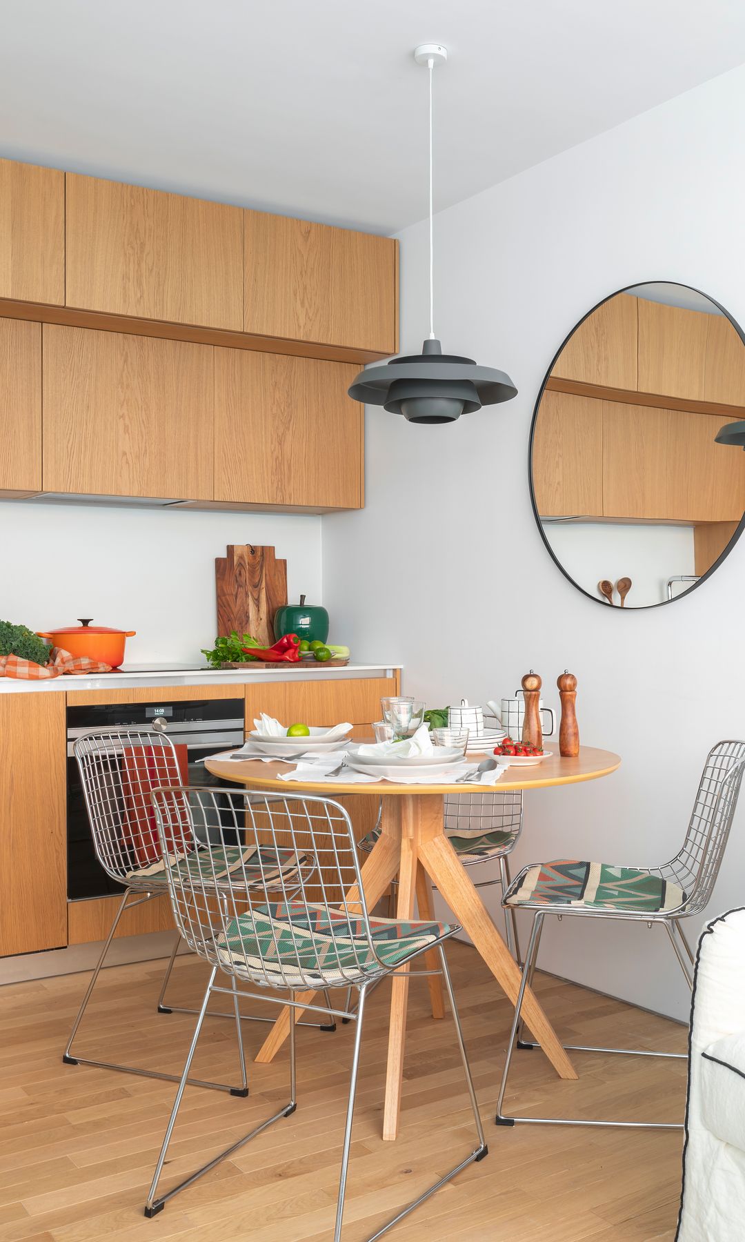 Cocina con comedor con mesa redonda de madera, sillas metálicas, espejo redondo, muebles de madera sin tirador 