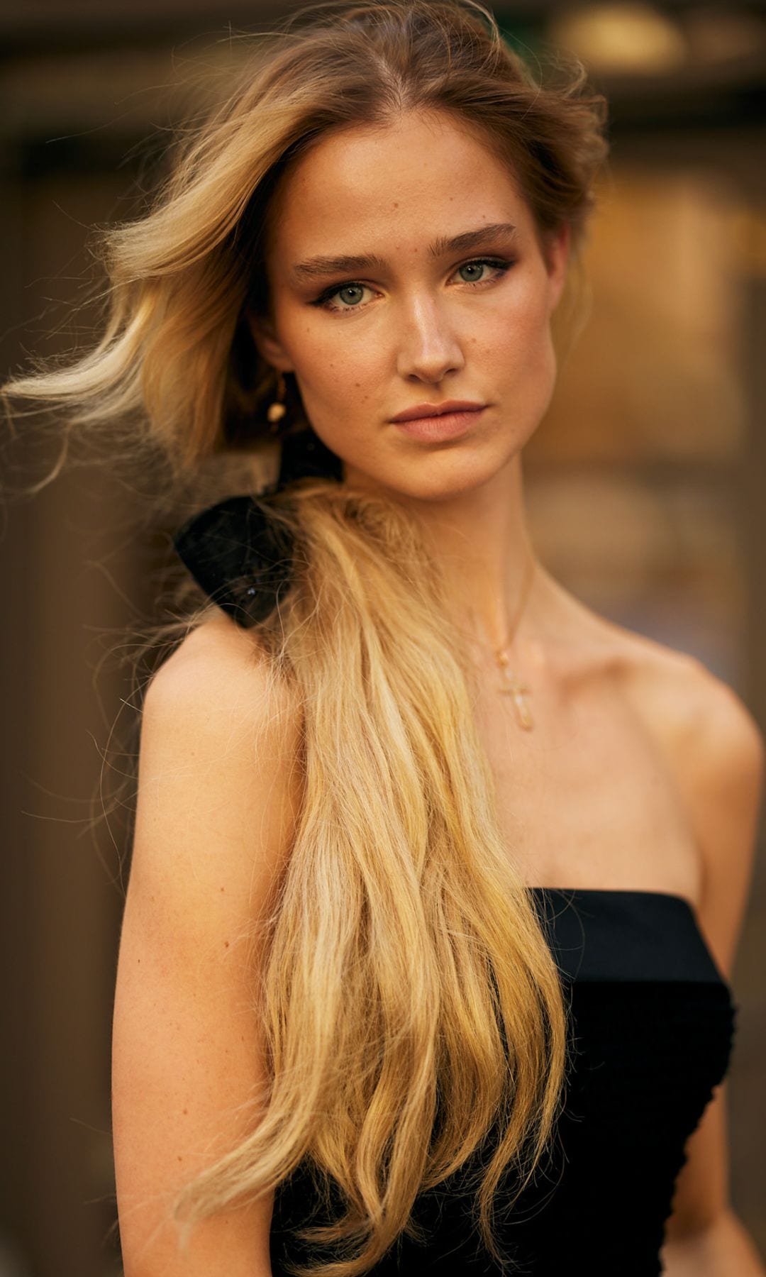 Mujer con coleta larga rubia, lazo negro y vestido palabra de honor negro en París