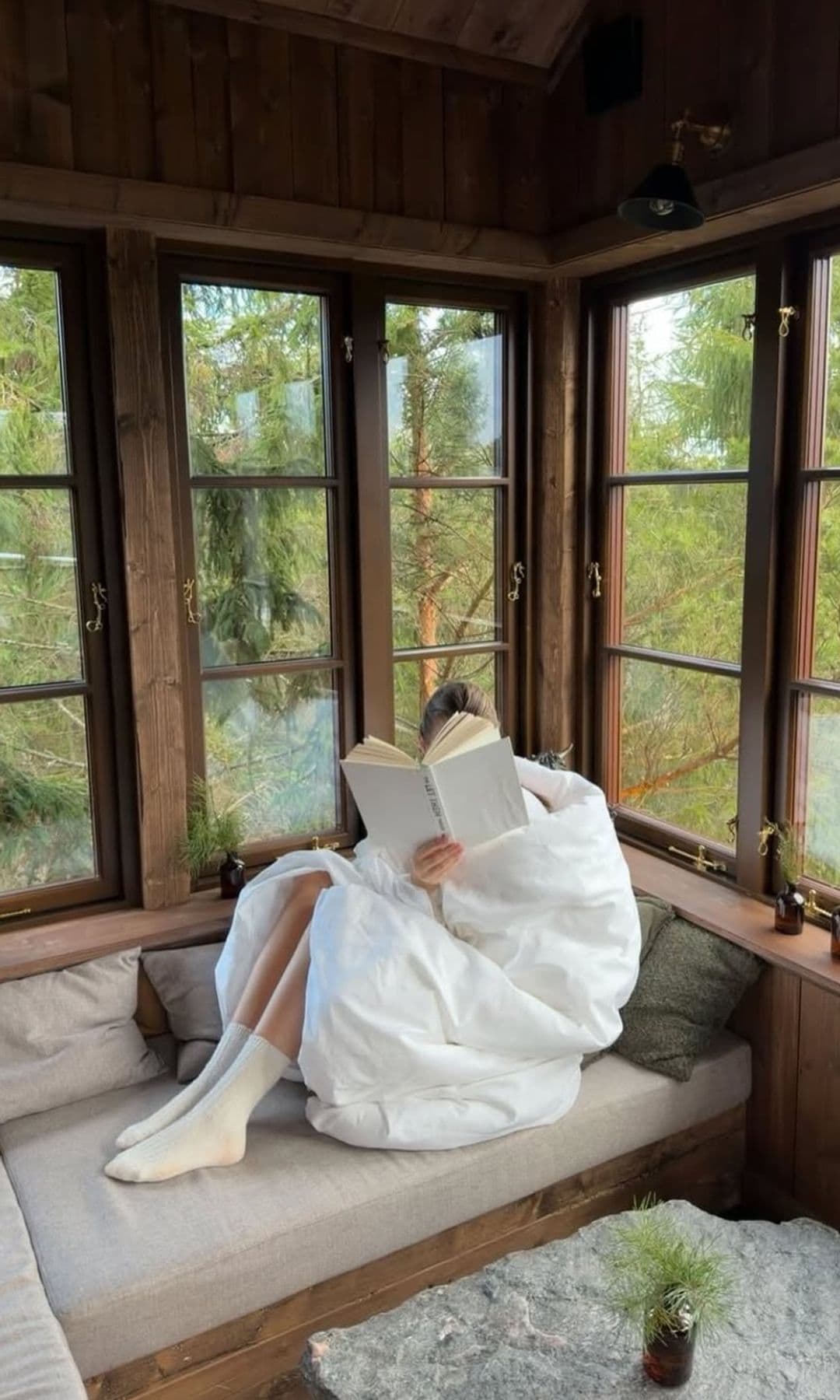 Una chica envuelta en un edredón leyendo al lado de su ventana