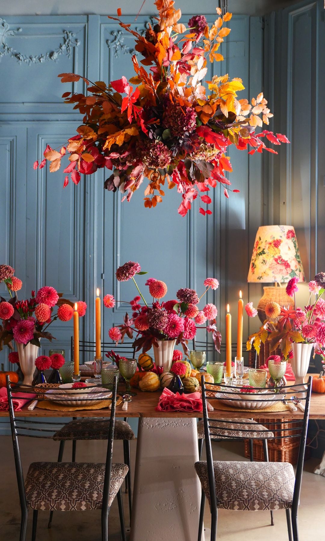 Mesa de comedor con arreglo floral en el techo, sillas de hierro con asiento tapizado, jarrones con flores, candelabros 