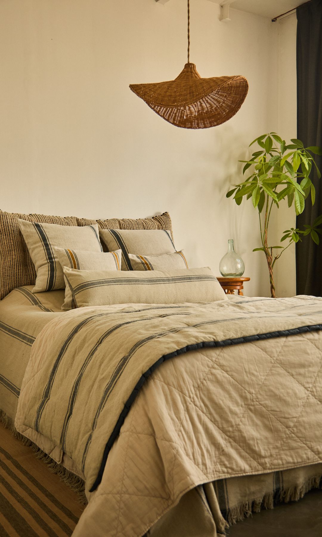 Dormitorio con lámpara de techo de fibras vegetales, ropa de cama de lino, planta, alfombra
