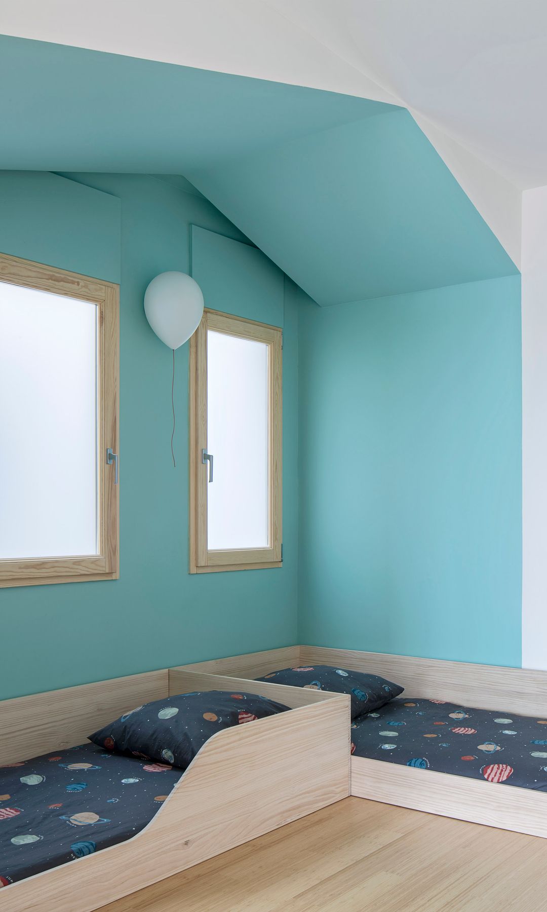 Habitación infantil con dos camas en L, pared en azul cielo, ventanas, con el marco de madera, aplique de pared en forma de globo