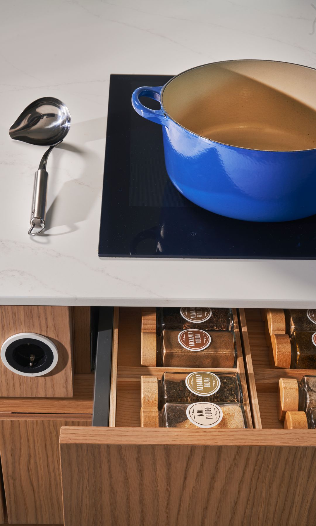 Cocina con cazuela azul en la placa y cajón abierto con tarros de especias 