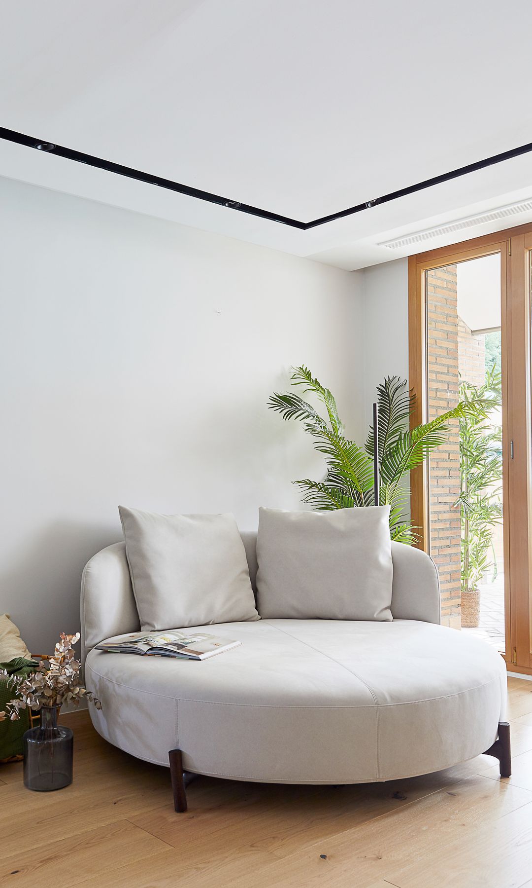 Rincón junto a la ventana con sillón redondo a modo de cama, suelo de madera, planta altas, cojines, lurz perimetral techo