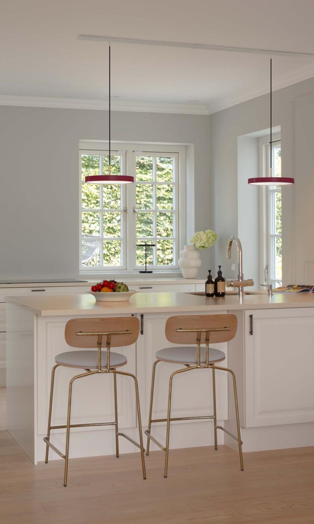 Cocina con península con taburetes de madera, lámparas de techo, muebles blancos y suelo de madera