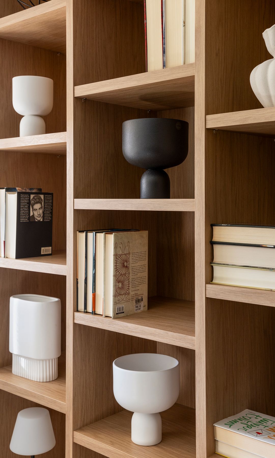 Estantería de madera con libros y piezas de cerámica blancas y negras 