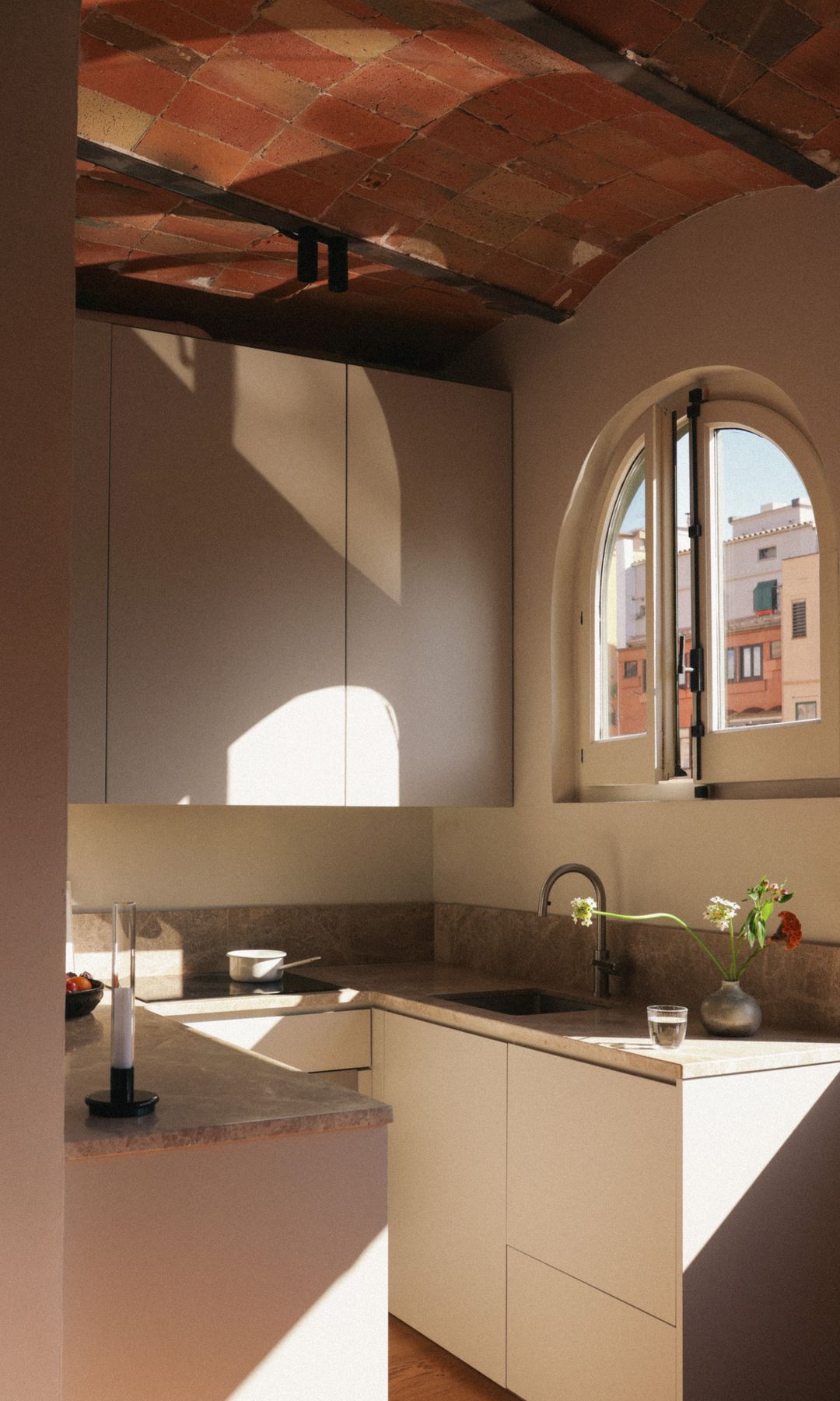 Cocina pequeña con luz natural, techo de bóvedas catalanas, focos negros en el techo, muebles beige