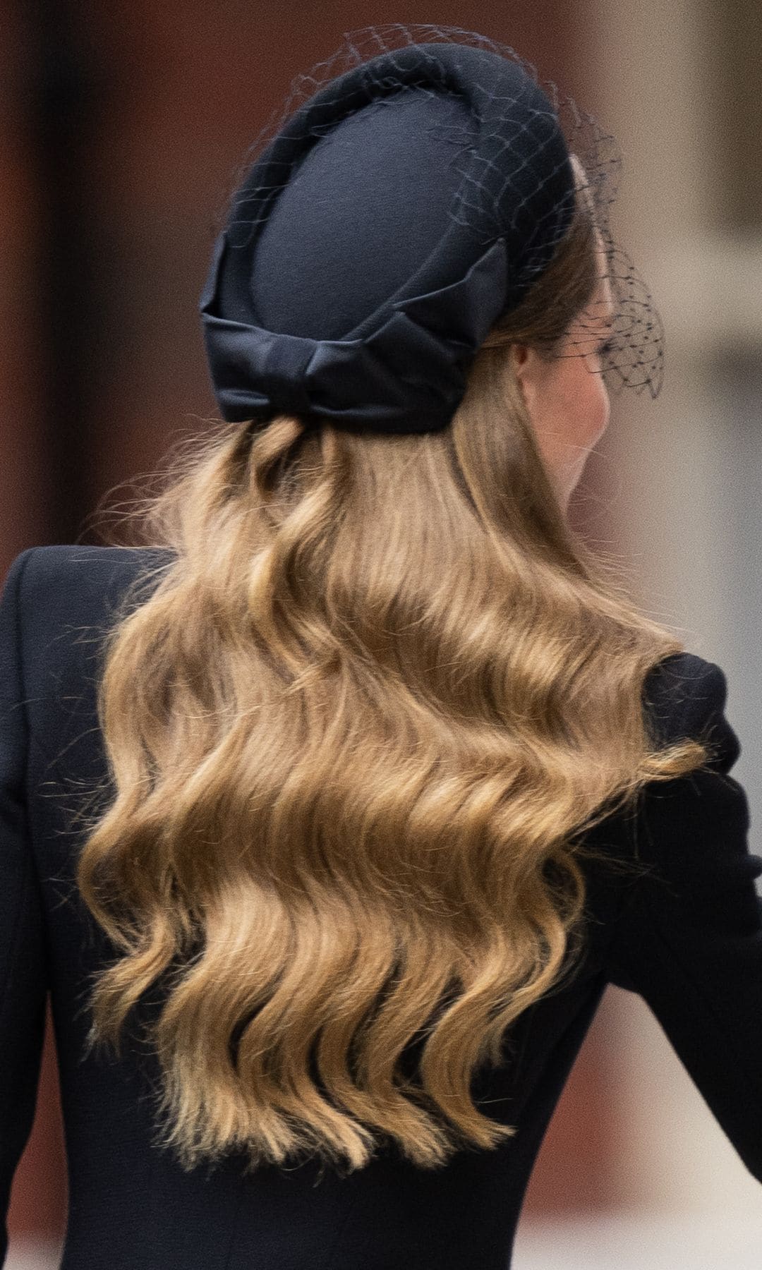 Kate Middleton de espaldas con tocado, vestido negro y melena suelta con ondas al agua