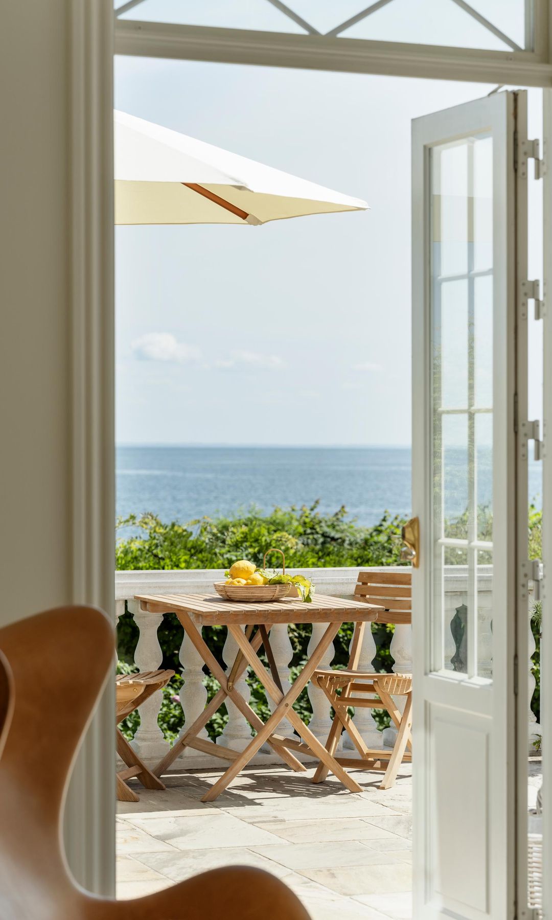Vista de la terraza desde el interior con mesa de madera, sillas de madera y sombrilla blanca