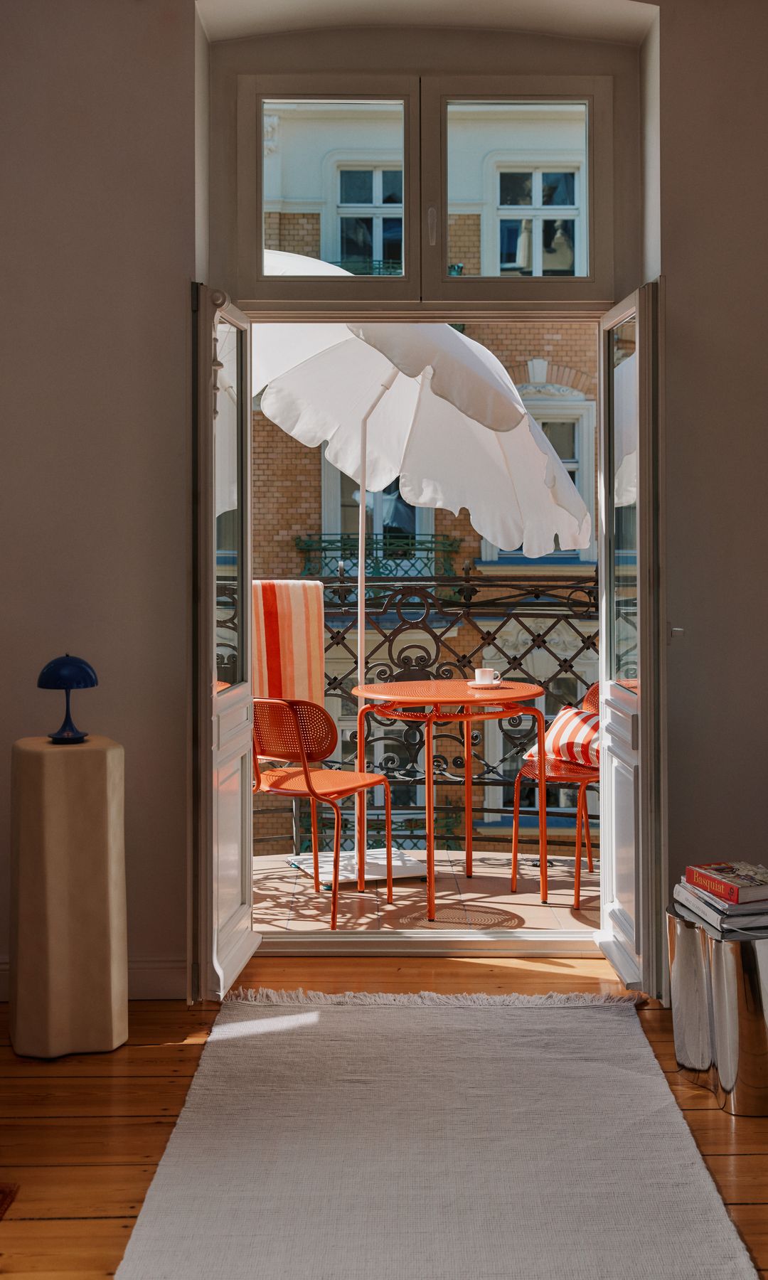 Balcón con mesa y sillas metálicas de color naranja, sombrilla blanca 