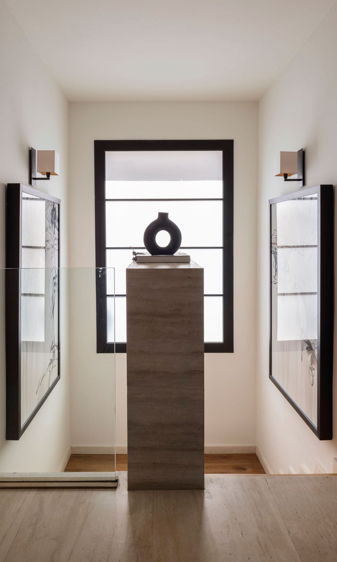 Subida de la escalera con barandilla de cristal, escalones de madera, cuadros, pedestal con escultura en el descansillo